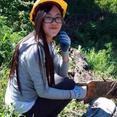 A volunteer wearing a hardhat, using a handsaw on a small log.