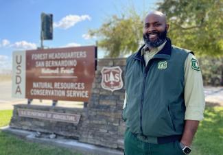 Bearded man in Forest Service uniform beside national forest sign