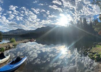 Two kayaks sit in lake with mountains and forest in background