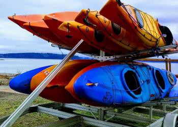 Orange and blue kayaks on a trailer with water in background